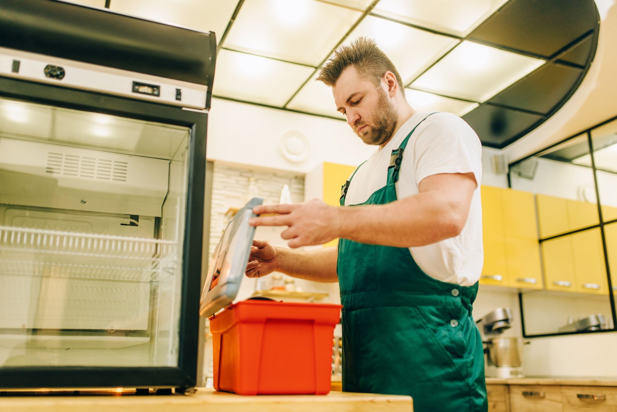 Worker with toolbox repair refrigerator at home