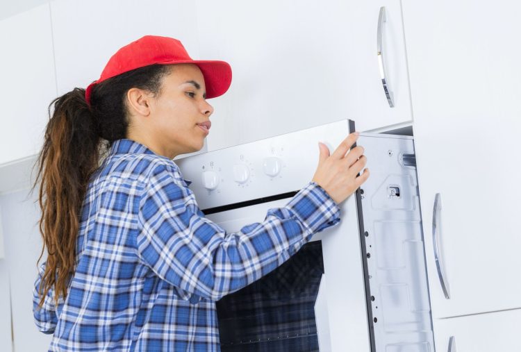female worker repairing oven in clients kitchen