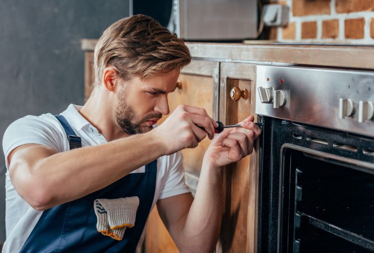 handsome young repairman fixing oven with screwdriver